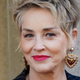Sharon Stone smiles wearing large, heart shaped earrings.